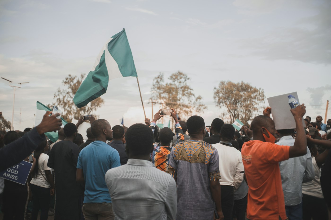 A crowd gathered in an open field, some waving Nigerian flags